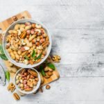 Different types of nuts in bowls with green leaves.